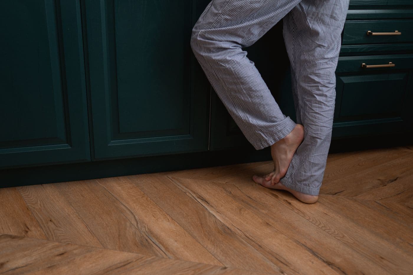 Bare feet on a warm wooden floor in front of dark green kitchen units
