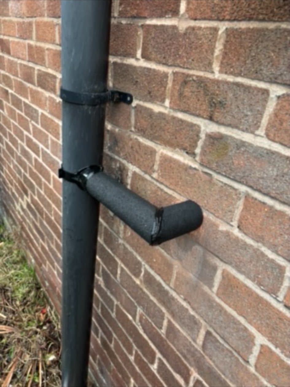 A condensate pipe joining a drainpipe on an outside brick wall, wrapped in weatherproof insulation
