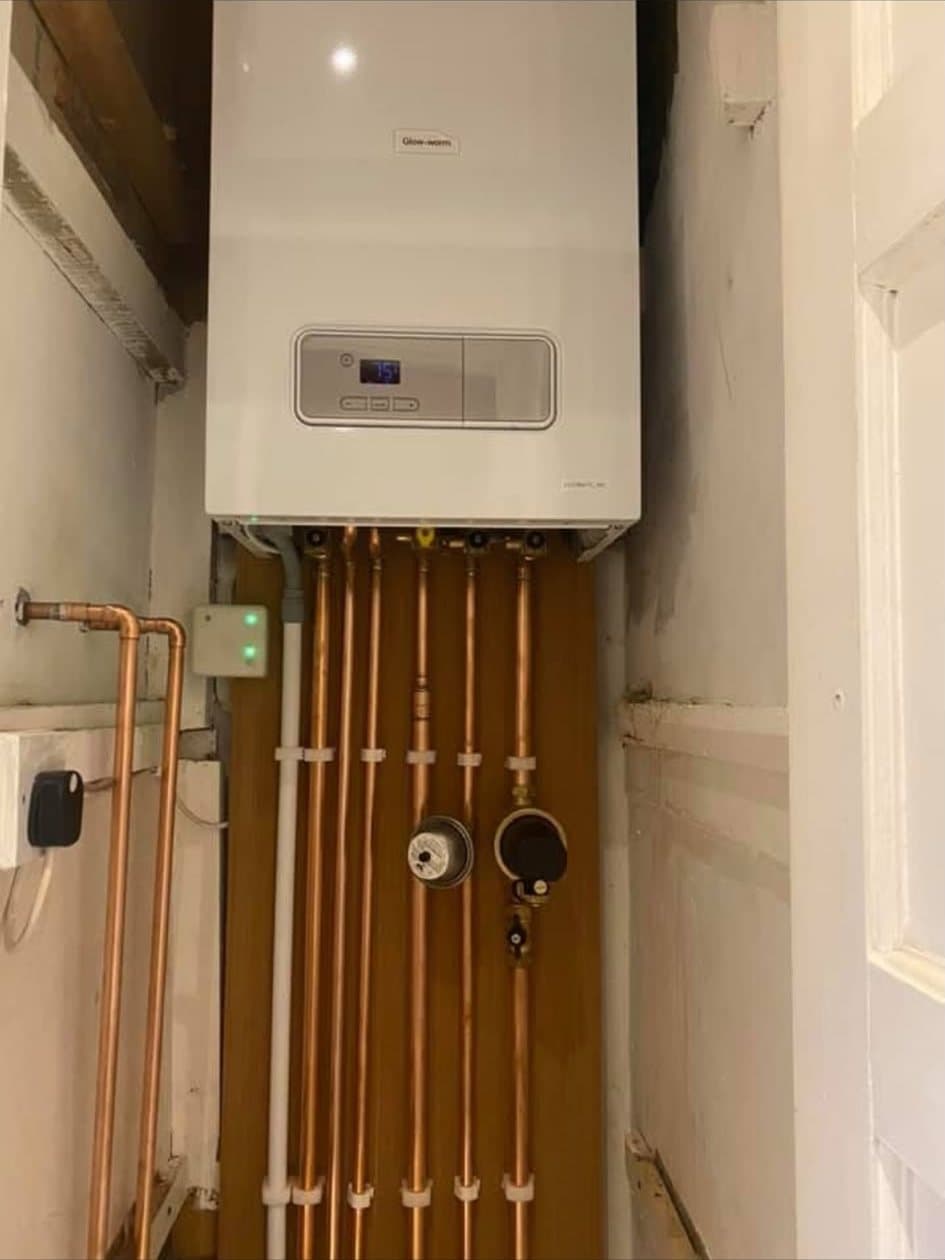 A new boiler in a cupboard with its copper pipework running straight down a timber backboard in evenly clipped rows