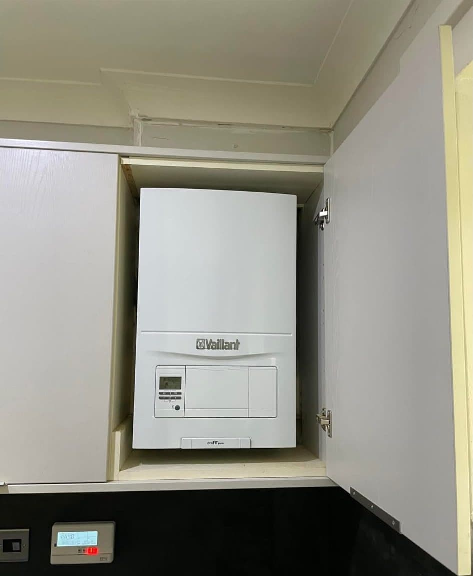 A Vaillant boiler fitted inside a kitchen wall cupboard, with its programmer on the wall beneath