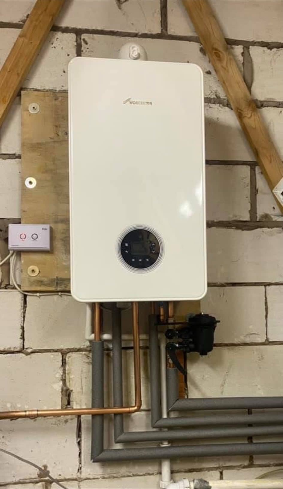 A new Worcester Bosch boiler on a blockwork loft wall, with a system filter and lagged pipework running away beneath it